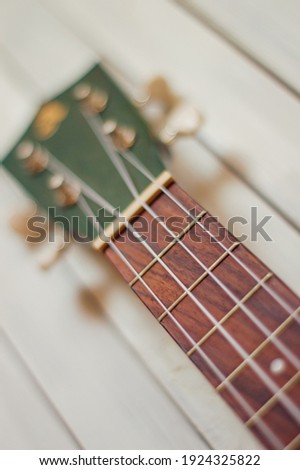 Close up of acoustic ukulele; ukulele strings, saddle, soundhole, ukulele body, neck, fretboard. Fretted folk instrument, wooden, inlay.
