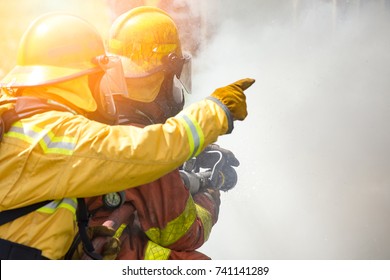 close up action of two firefighters water spray by high pressure nozzle to fire surround by smoke with flare and copy space