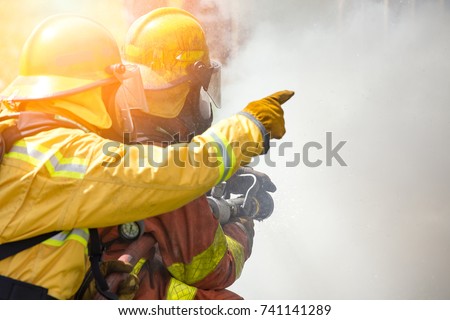 close up action of two firefighters water spray by high pressure nozzle to fire surround by smoke with flare and copy space