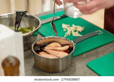 Close up of adding liquid from spoon into pot with sliced pears on green cutting board in kitchen.