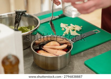 Close up of adding liquid from spoon into pot with sliced pears on green cutting board in kitchen.