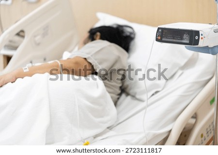 Close up adjust infusion pump set iv fluid intravenous drop saline drip with blurry patient woman on hospital bed in hospital room.Medical treatment emergency patient concept