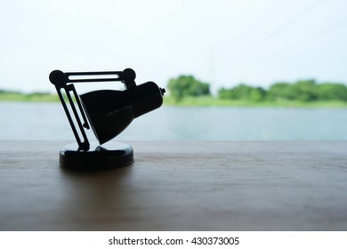 close up of adjustable mini small LED desk table lamp bent or stoop his body on the floor and feeling lonely on the wooden table near the river or canal.