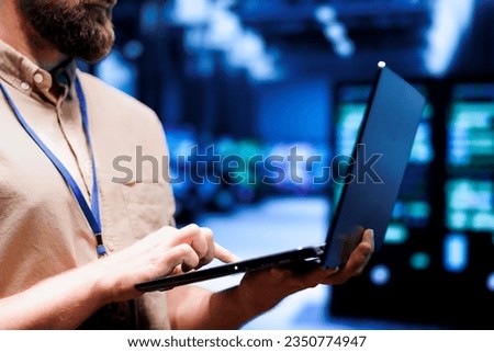 Close up of admin using laptop to check electronics in blockchain technology application specific integrated circuit server rig clusters. Focused employee checking for issues in crypto mining farm