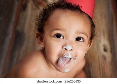 Close up of an adorable baby boy with cake icing all over his face and his tongue sticking out. - Powered by Shutterstock