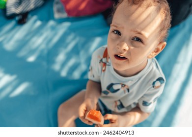 Close up of an adorable little boy eating watermelon on a beach on sunny summer day. A cute child is sitting and eating fruit while making eye contact with camera. Top view of a boy eating watermelon. - Powered by Shutterstock