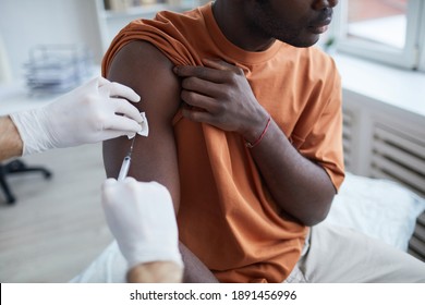Nahaufnahme eines erwachsenen afroamerikanischen Mannes, der wegschaut, während er im Krankenhaus oder Krankenhaus einen Kokosimpfstoff erhält, wobei die männliche Krankenschwester Impfstoff in die Schulter injiziert