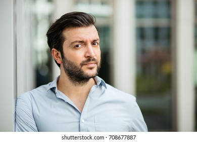 Close Up Of An Adult Man In Blue Shirt Outside, Having An Office Building Behind