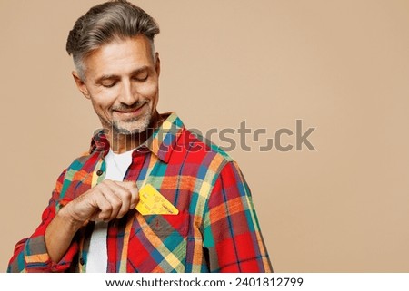 Close up adult man wear red shirt white t-shirt casual clothes hold put mock up of credit bank card into pocket isolated on plain pastel light beige color background studio portrait. Lifestyle concept