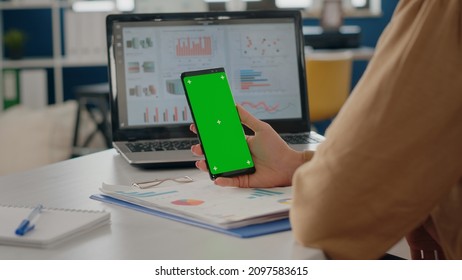 Close Up Of Adult Vertically Holding Phone With Green Screen In Startup Office. Business Woman Using Smartphone With Chroma Key Display On Isolated Mock Up Background And Template.