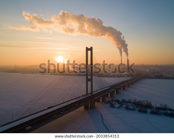 Close up aerial\
of bridge silhouette over frozen lake or river at dawn (sunset).\
Cars and trucks riding\
highway