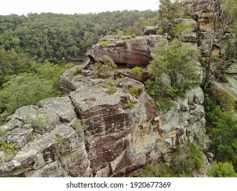 Close Up Aerial View Of Cliff Top With Lush Green Trees Growing Out Of Rock Face And Brown Lake In Background, Overcast Lighting. Rough Grey Australian Bush Rock, Limestone. 