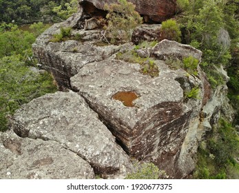 Close Up Aerial View Of Cliff Top With Lush Green Trees Growing Out Of Rock Face And Brown Lake In Background, Overcast Lighting. Rough Grey Australian Bush Rock, Limestone. 