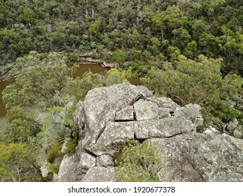 Close Up Aerial View Of Cliff Top With Lush Green Trees Growing Out Of Rock Face And Brown Lake In Background, Overcast Lighting. Rough Grey Australian Bush Rock, Limestone. 