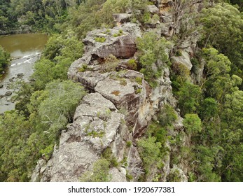 Close Up Aerial View Of Cliff Top With Lush Green Trees Growing Out Of Rock Face And Brown Lake In Background, Overcast Lighting. Rough Grey Australian Bush Rock, Limestone. 