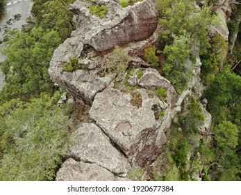 Close Up Aerial View Of Cliff Top With Lush Green Trees Growing Out Of Rock Face And Brown Lake In Background, Overcast Lighting. Rough Grey Australian Bush Rock, Limestone. 