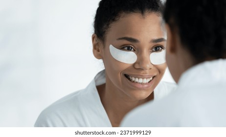 Close up of african America young woman look in mirror in bathroom use apply under eye cotton patches, smiling biracial female do beauty facial procedures in bath for healthy skin, skincare concept - Powered by Shutterstock