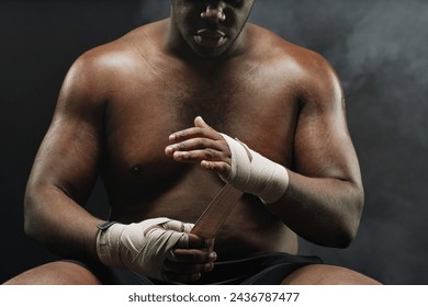 Close up of African American boxer wrapping hands with bandages preparing for fight against black background copy space - Powered by Shutterstock