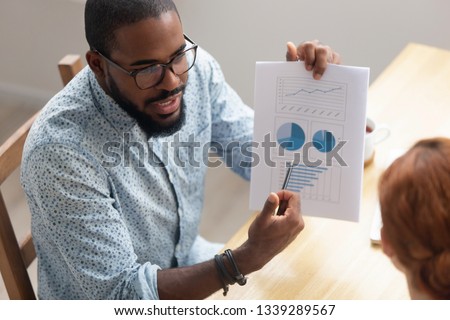 Close up African American businessman consulting client, holding document with graphs and diagram, mentor explaining business strategy to trainee, partners discussing project results