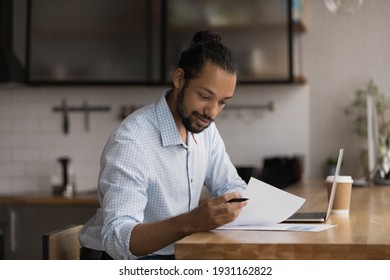Close up African American businessman reading document, working with correspondence, sitting at wooden table with laptop, entrepreneur accountant analyzing financial report, holding paper sheet