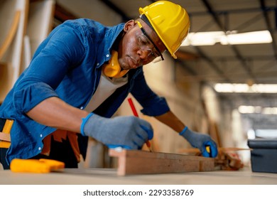 Close up African American carpenter man use pencil to mark on timber and work in factory for producing wood furniture or wood work. - Shutterstock ID 2293358769