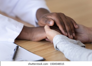 Close up African American doctor holding hands of female patient at hospital, expressing support and care, woman received bad news and medical checkup results, medical ethics and empathy