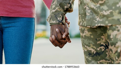 Close Up Of African American Male And Female Hands Holding Each Other Gently Outdoors. Man Soldier In Military Uniform Taking Hand Of Woman, His Girlfriend Or Wife. Happy Meeting Concept.