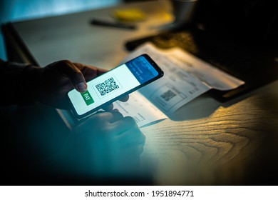 Close up of an African American male hand holding mobile phone with QR payment app on screen, at a desk with a laptop and a bill