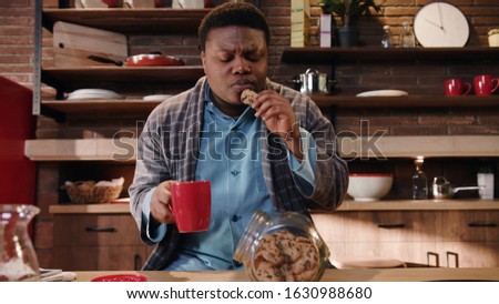 Close up african american man eat breakfast in the morning at home in kitchen drinks coffee and eating homemade cookies tasty feel happy fresh healthy house indoors sitting tea slow motion