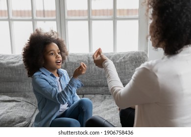 Close up African American mother teaching disabled daughter, showing symbols, little girl practicing sign language, repeating sounds, involved in speaking lesson with teacher at home, hearing loss - Powered by Shutterstock