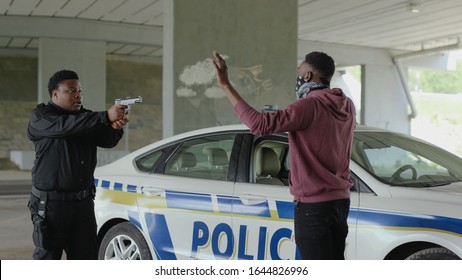 Close up african american policeman with pistol arrest offender in mask stand hands up in patrol car in handcuffs burglar crime hold danger gangster gun robber illegal law bad guy slow motion