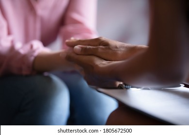 Close up African American psychotherapist holding clipboard, touching patient hands, expressing empathy and support at meeting, counselor therapist comforting girl during personal therapy session