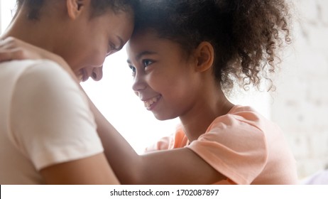 Close Up African American Teen Daughter Touching Forehead With Millennial Mother. Happy Smiling Diverse Family Looking At Each Other And Embracing Together. Mom And Child Sweet And Cute Hugging.