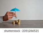 Close up of african american woman hand holding blue umbrella over stack of coins on table. Hands of financial advisor saving money. Businesswoman protect saving and money with copy space.