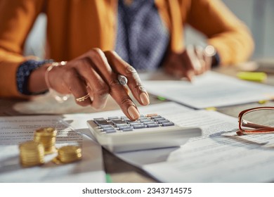 Close up of african american woman hands calculating tax while working at desk. Casual businesswoman using calculator to check monthly income and expenses of her freelance activity.  - Powered by Shutterstock