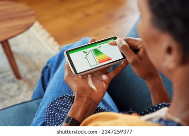 Close up of african american woman holding smartphone with energy efficiency chart and class on screen. Black female hands holding smart phone and looking at house efficiency rating. - Powered by Shutterstock