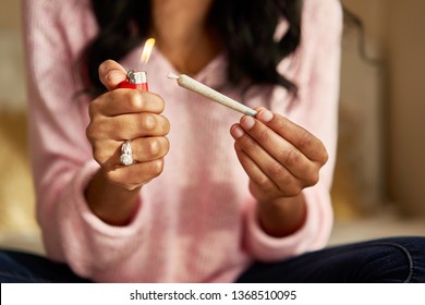 close up of african american woman lighting marijuana joint at home