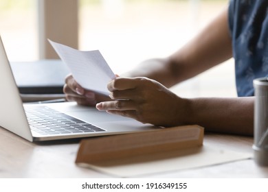 Close up African American woman reading letter at home, sitting at table with open envelope and laptop, businesswoman working with correspondence, received information from bank or college - Shutterstock ID 1916349155