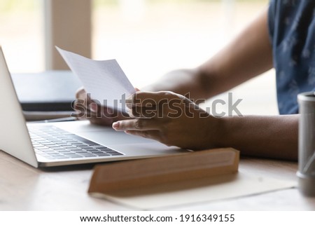 Close up African American woman reading letter at home, sitting at table with open envelope and laptop, businesswoman working with correspondence, received information from bank or college