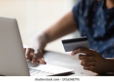 Close up African American woman shopping purchasing online, using laptop, typing, entering information, checking balance, browsing internet banking service, paying by credit card, making payment