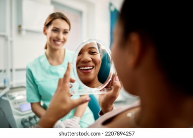 Close up of African American woman using mirror while looking at her teeth after dental check up at dentist's. - Powered by Shutterstock