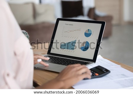 Close up African American woman working financial project with statistics, using laptop and calculator, preparing presentation for report, calculating bills or investments, planning managing budget
