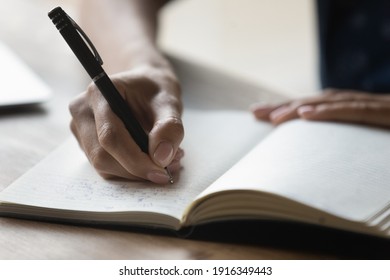 Close up African American woman writing in notebook, holding pen, businesswoman entrepreneur planning workday, meetings, managing time, student taking notes, preparing for exam, handwriting - Powered by Shutterstock