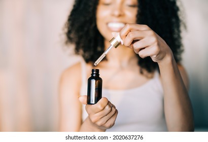 Close up african american young woman holding brown glass bottle with spa cosmeticsat hone. Beauty blogging, salon therapy, self skin care, mockup, minimalism concept