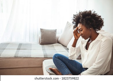 Close up african female sit on couch feels unhappy desperate thinking about personal difficulties mental health problems, 30s sad woman need psychological support goes through divorce break up concept