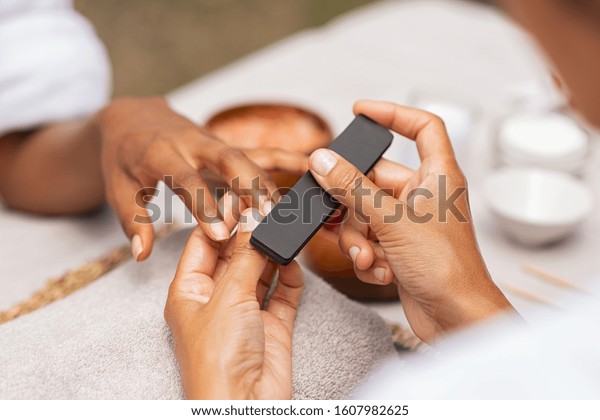 Close up of african\
hands of a qualified manicurist filing the nails of a young woman.\
Hands during manicure care session. Detail of a girl in a nail\
salon receiving manicure.
