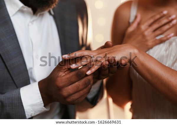 Close up of african man in love putting wedding\
ring on his woman finger
