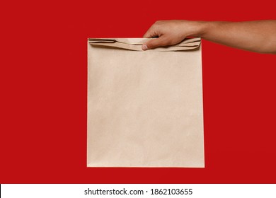 Close up african man male hold in hand brown clear empty blank craft paper bag for takeaway isolated on red background. Packaging template mockup. Delivery service concept. Copy space Advertising area - Powered by Shutterstock