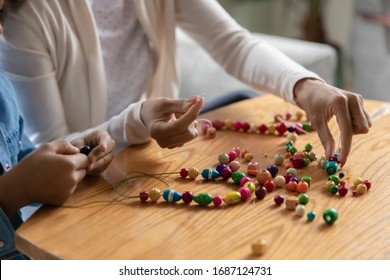 Close up african mom and daughter making handmade bangles, charms using cord and wooden natural material diverse color beads improve fine motor skills and promote coordination pastime activity concept - Shutterstock ID 1687124731