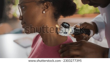 Close Up of an African Skin Care Professional Using a Dermatoscope to Examine Neck Tissue on the Skin of a Young Black Female During a Health Check Visit to a Clinic. Dermatologist in Hospital